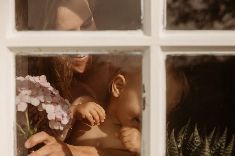 photographie d'une mère et son bébé dans leur maison en train de regarder par la fenêtre